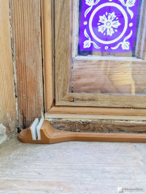 Closeup of a stripped wood sash window fitted with colour matched WindowSkins secondary glazing and subframe. A venting arms sits on the sill.