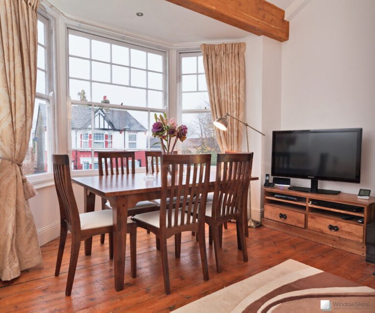 Wide view of dining table with three sash window, fitted with WindowSkins secondary glazing, visible in the background