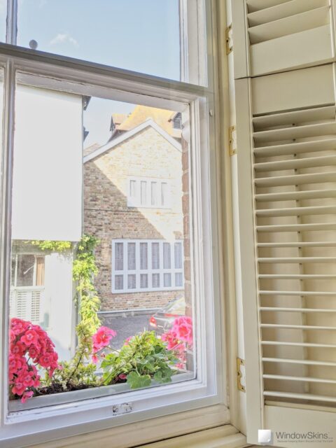 Closeup of WindowSkins magnetic secondary glazing, with split panel and subframe, fitted to a cream sash window with cream plantation shutters