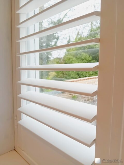 Closeup of plantation shutter door, with louvres open, overlaying WindowSkins magnetic secondary glazing installation