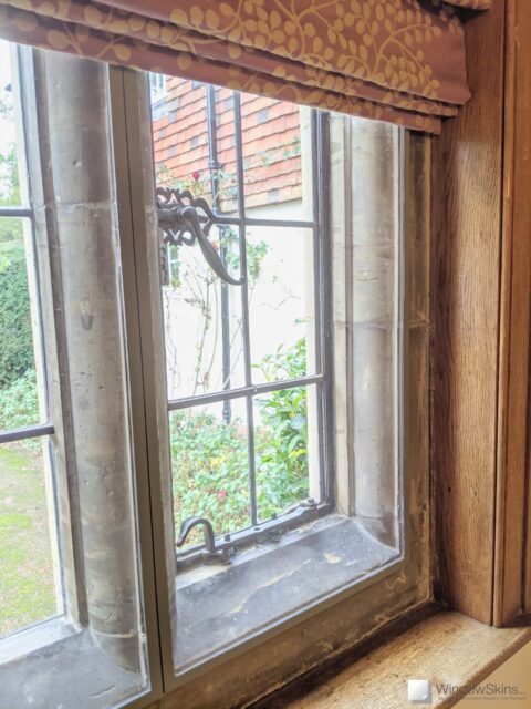Closeup of colour matched secondary glazing retrofit to listed property stone mullion with metal windows and leaded lights