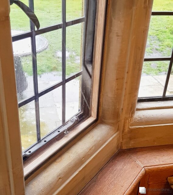 Closeup of an oak timber subframe and dark brown magnetic secondary glazing panel fitted to a stone mullion window recess