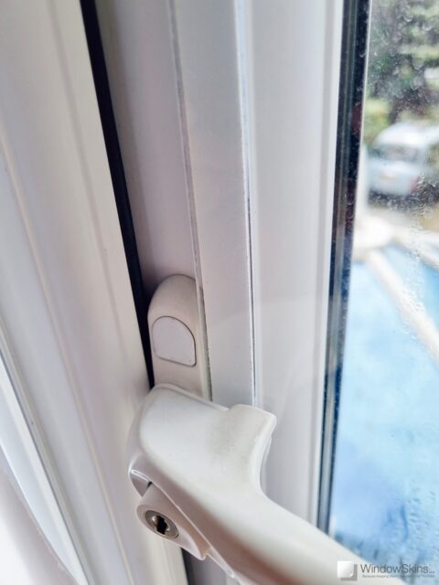Close-up of a magnetic triple glazing panel retrofit to a double glazed uPVC window. The window handle can be seen in the open position, demonstrating adequate space for the glazing panel to fit underneath without causing an obstruction